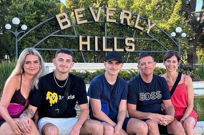En grupp människor sitter på en bänk framför en skylt där det står ”BEVERLY HILLS”. 3