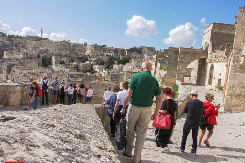 A group of tourists walking along a stone pathway with a historic cityscape in the background. 1