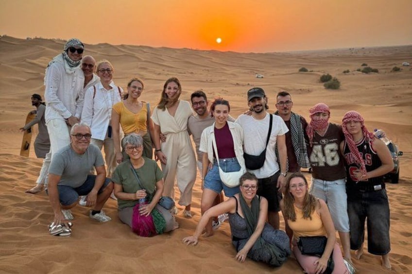 Un gruppo di persone che posano su una spiaggia sabbiosa, con un tramonto sullo sfondo. 4