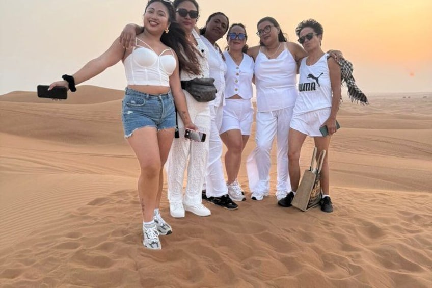 Un gruppo di persone vestite di bianco che posa su una duna di sabbia con un tramonto sullo sfondo. 1