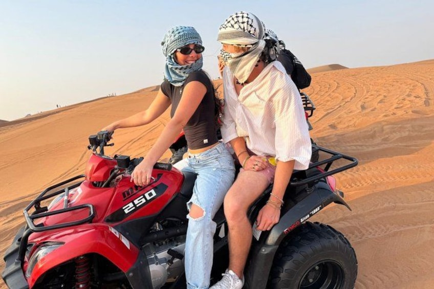 Due persone su un quad rosso in un deserto con dune di sabbia sullo sfondo. 2