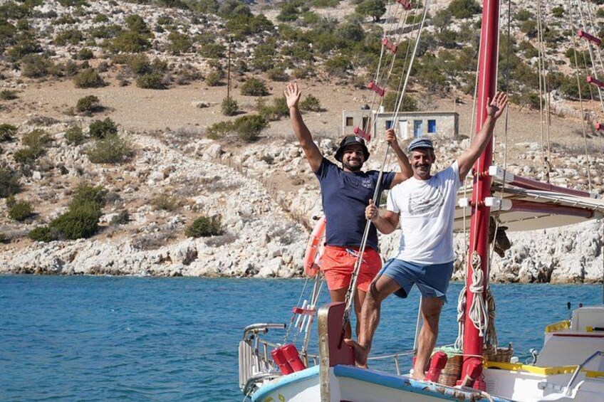 Two people on a sailboat with a rocky coastline in the background. 3