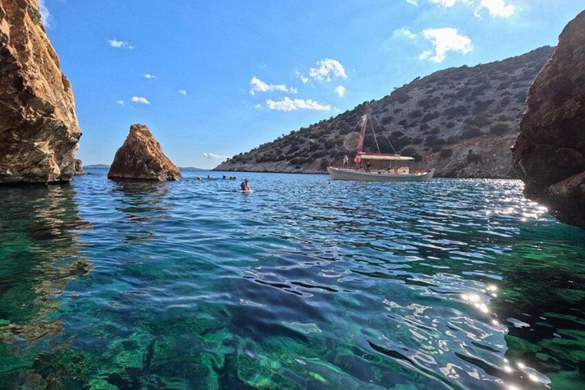 Mar azul y transparente con una costa rocosa, un velero y un edificio pequeño. 5