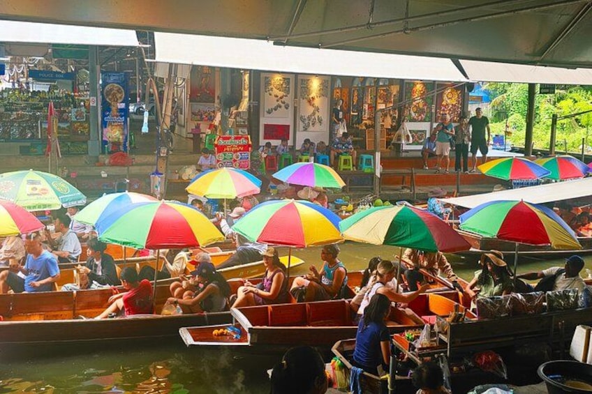 A waterway with boats and colorful umbrellas, people sitting and standing, and a market in the background. 4