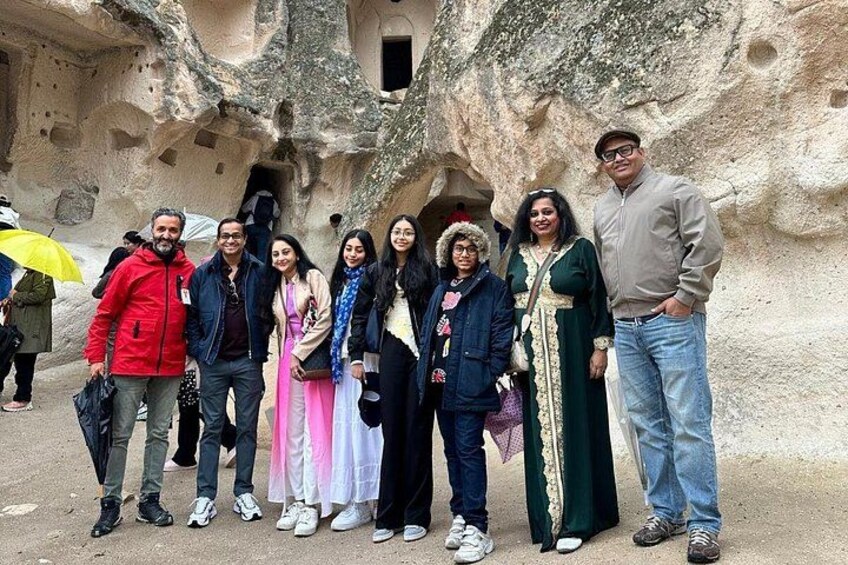 A group of people standing in front of a cave-like structure with rock formations. 1