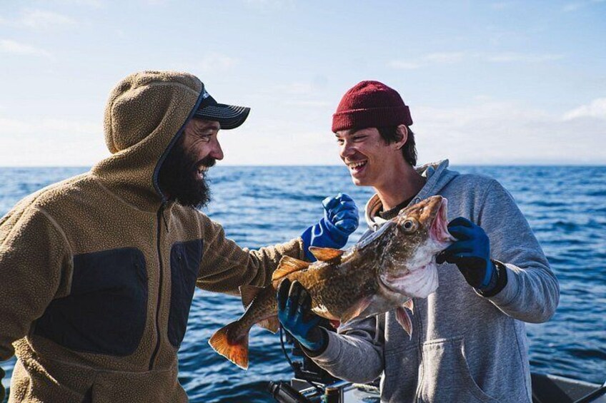 Twee mensen houden een vis vast op een boot, met de oceaan op de achtergrond. 5