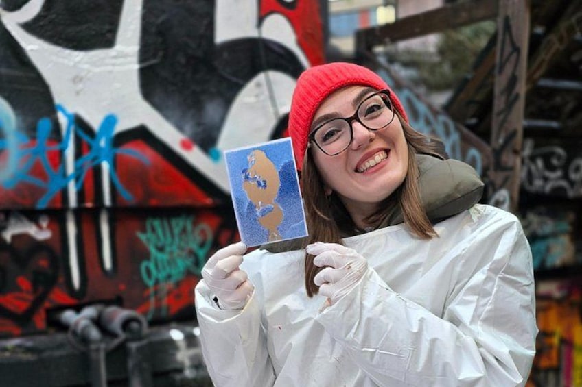 Eine Person hält eine Karte mit blau-weißem Design vor einer mit Graffiti besprühter Wand. 5
