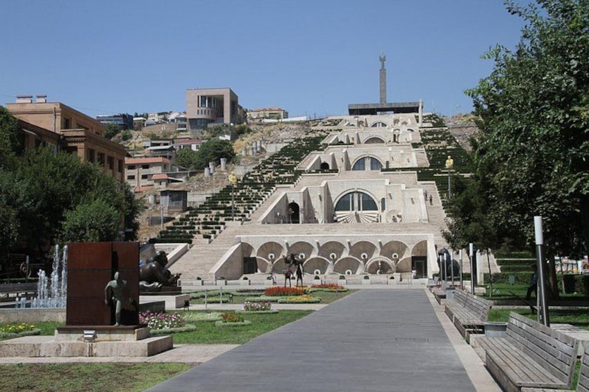 A staircase leading to a building with a unique architectural design, surrounded by a park with benches and a fountain. 2