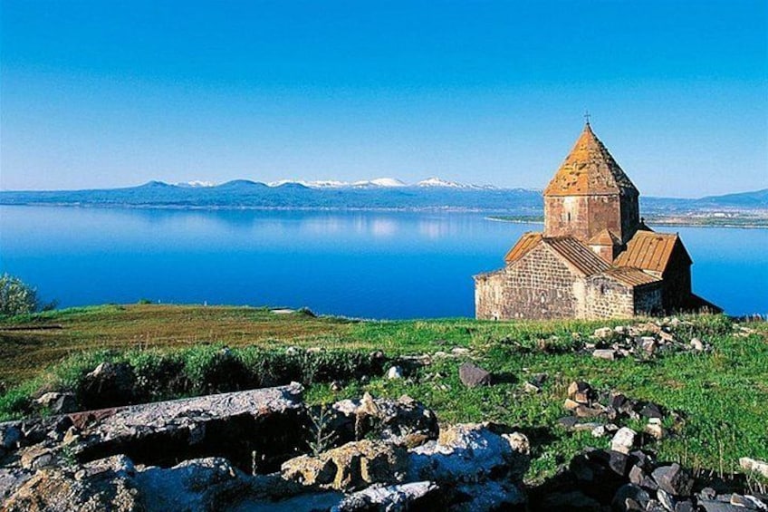 A stone church with a conical roof by a calm lake with mountains in the background. 3