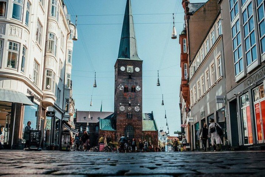 A cobblestone street with a tall clock tower, buildings, and hanging lights. 3