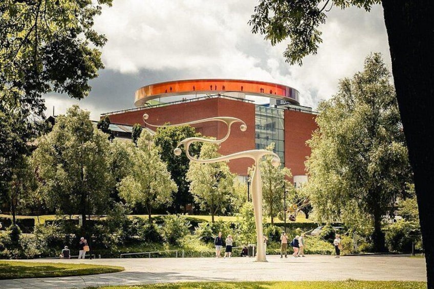 A modern building with a circular design, surrounded by trees and a park with people walking. 4