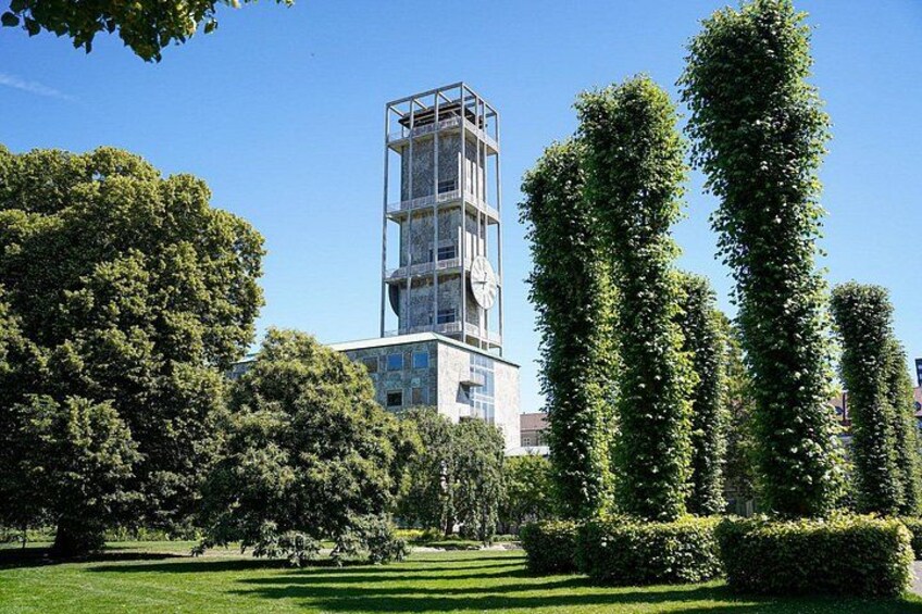 A modern building with a clock, surrounded by well-maintained hedges and trees. 2