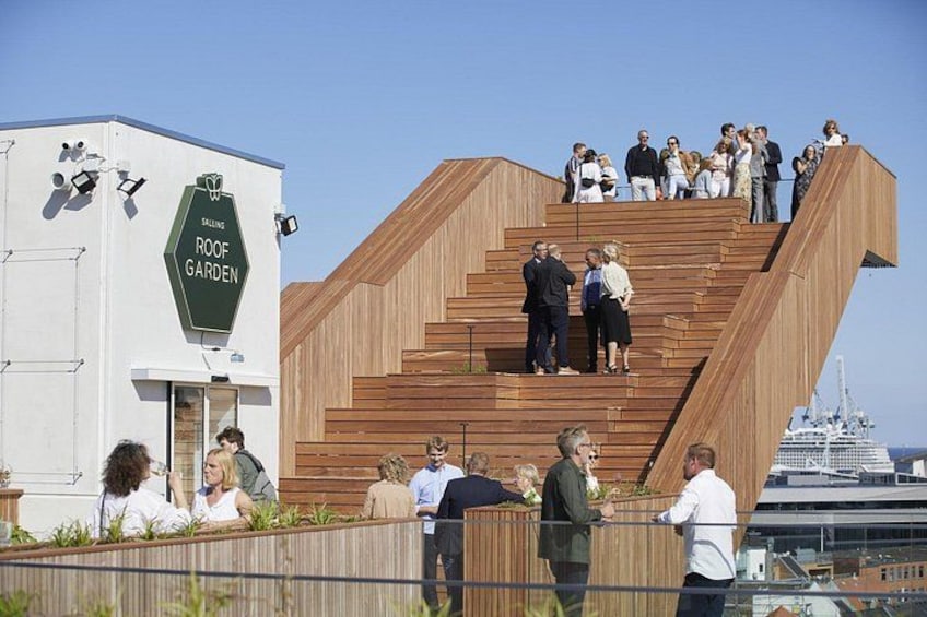 A wooden staircase leading to a rooftop garden with people walking around. 2