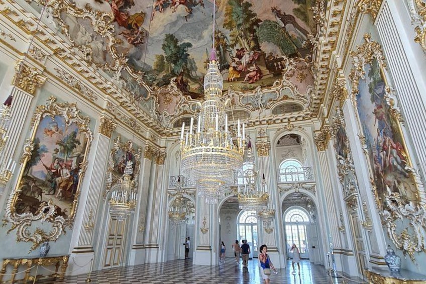 An ornate interior with a grand chandelier, detailed frescoes, and classical architecture. 3