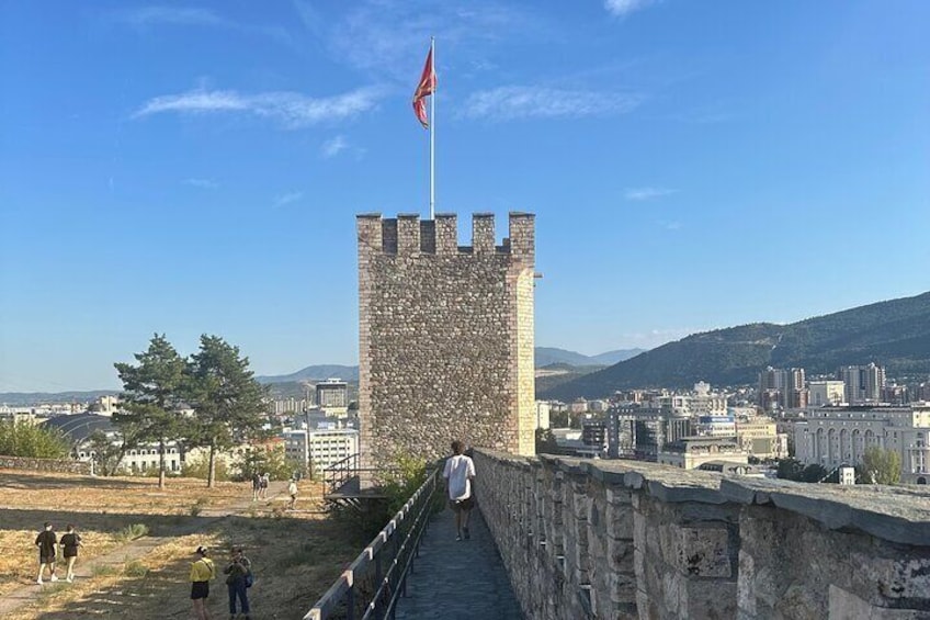 Ein Steinturm mit einer Flagge, einem gepflasterten Weg und einer Stadtlandschaft im Hintergrund. 2