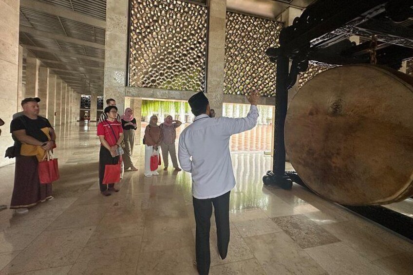 A group of people in a spacious indoor area with a large gong and a decorative wall. 5