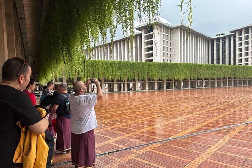 A group of people taking photos in front of a modern building with a tiled floor and hanging greenery. 4