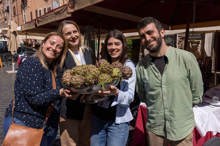 A group of people holding a tray of artichokes in an outdoor market setting. 3