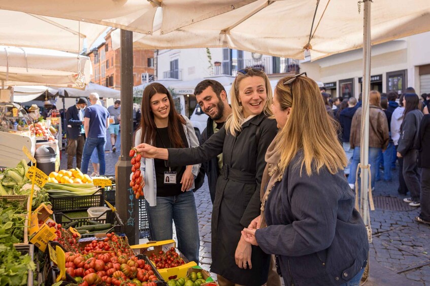 A group of people at an outdoor market with various fruits and vegetables on display. 5