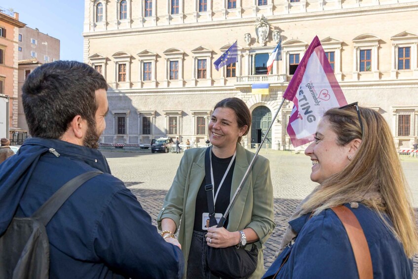 Three people conversing in front of a historic building with flags. 5