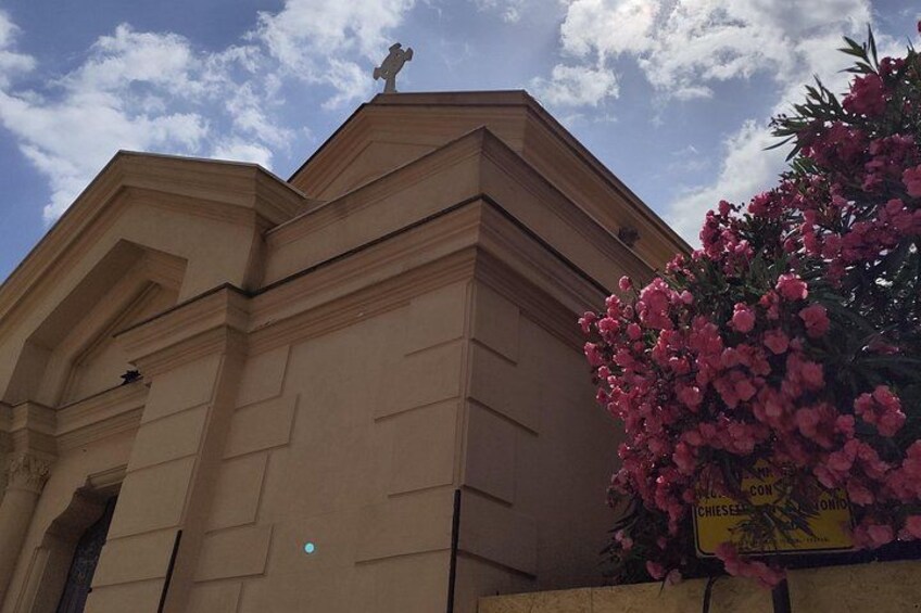 A building with a cross on top, a flower box with pink flowers, and a sign with text. 4