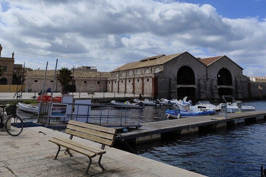 A waterfront with boats docked, a bench, and a historic building with arches. 5