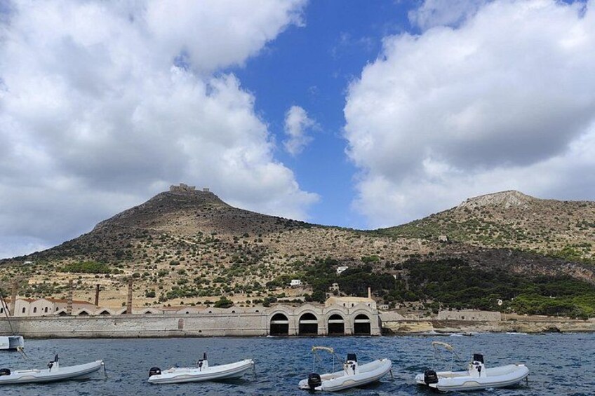 A coastal landscape with boats on the water, a hill with ruins, and a clear sky. 1