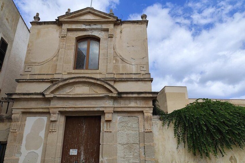 A historic building with a central arched doorway, a window above it, and a small bell tower. 3