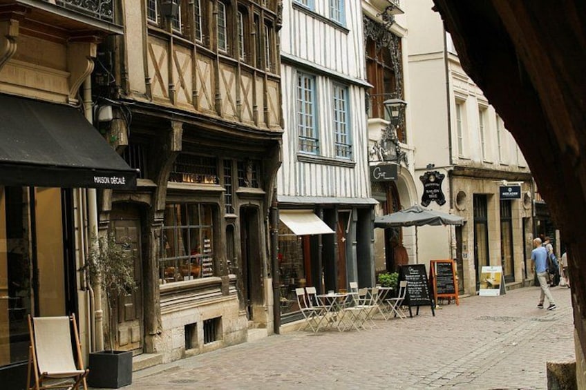 En brostensbelagt gade med historiske bygninger, en café kaldet 'Mason Decalé', og en person i det fjerne. 5