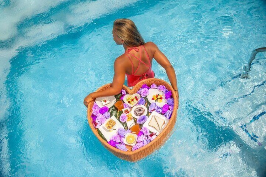 A woman in a heart-shaped basket floating in a pool with flowers and food. 4