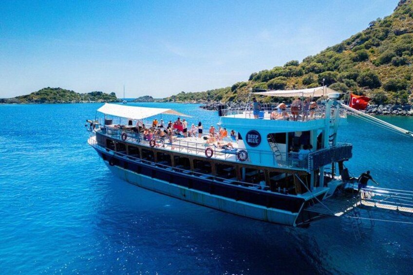 A large boat with people on board, a clear blue sea, and a hilly landscape in the background. 2