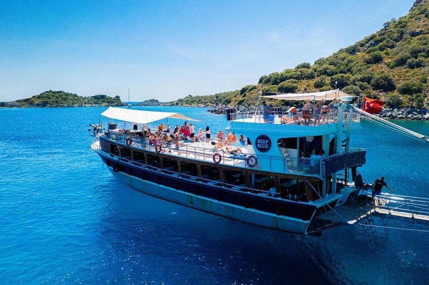 A boat with people on board, a clear blue sea, and a hilly landscape in the background. 2