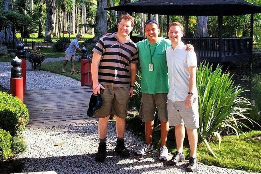 Three people standing on a gravel path with a wooden bridge in the background. 5