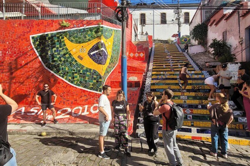 A mural of the Brazilian flag on a red wall, a staircase, and people walking. 4