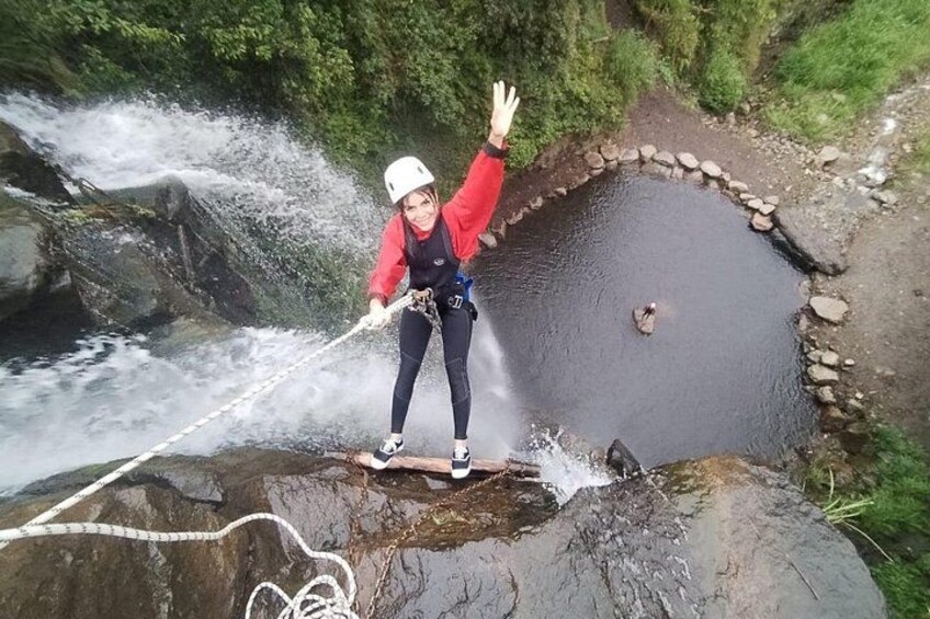 A person on a narrow rock ledge with a rope, near a waterfall. 5