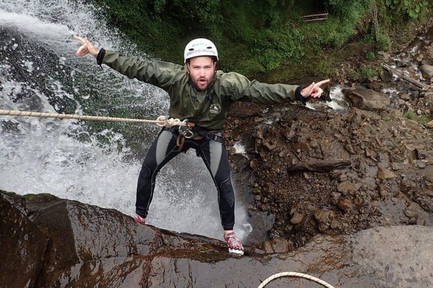 A person rappelling down a rocky cliff with a rope, surrounded by water and greenery. 3