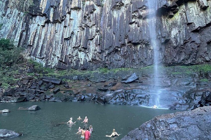Una cascada, acantilados rocosos y personas nadando en una poza natural. 5