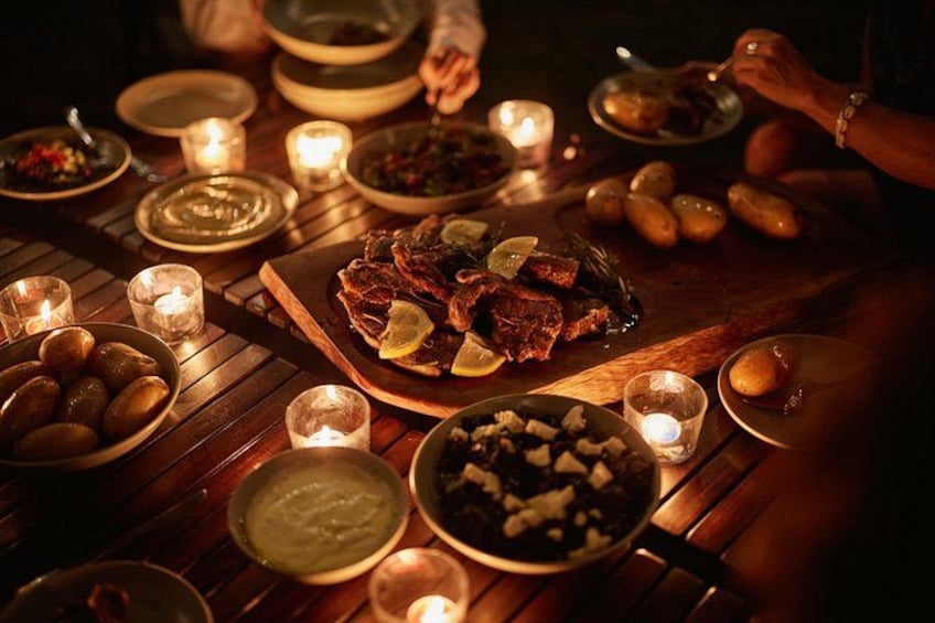 Una mesa de madera con varios platos, incluyendo carne asada, patatas y cuencos de comida, iluminada por velas. 2