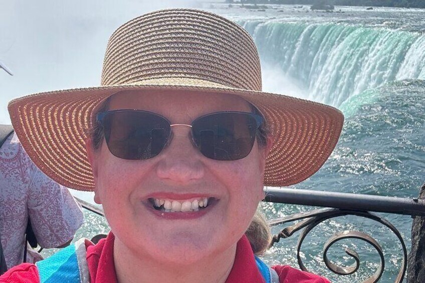 A person wearing a straw hat and sunglasses, with a waterfall in the background. 2
