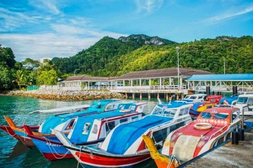 A dock with colorful boats, a pier, and lush green hills in the background. 1