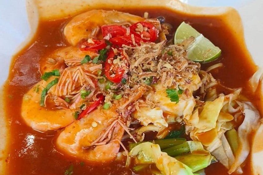 A bowl of soup with shrimp, vegetables, and a lime wedge. 5