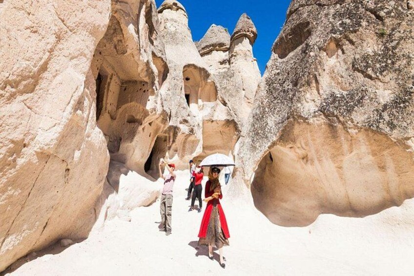 A person in a red dress walking through a rock formation with large, rounded caves. 2
