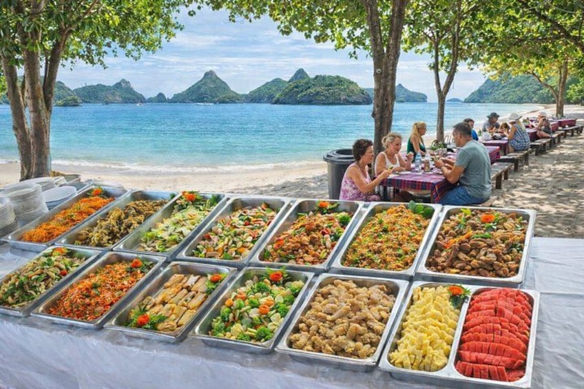 A buffet table with various food items, a beach with people dining, and a scenic view of the ocean and mountains in the background. 5