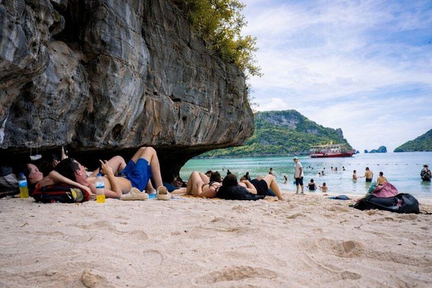 A beach with people sunbathing and swimming, a large rock formation, and a boat in the water. 4