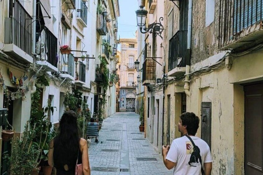 Una calle estrecha flanqueada por edificios, algunos con balcones y plantas. 3