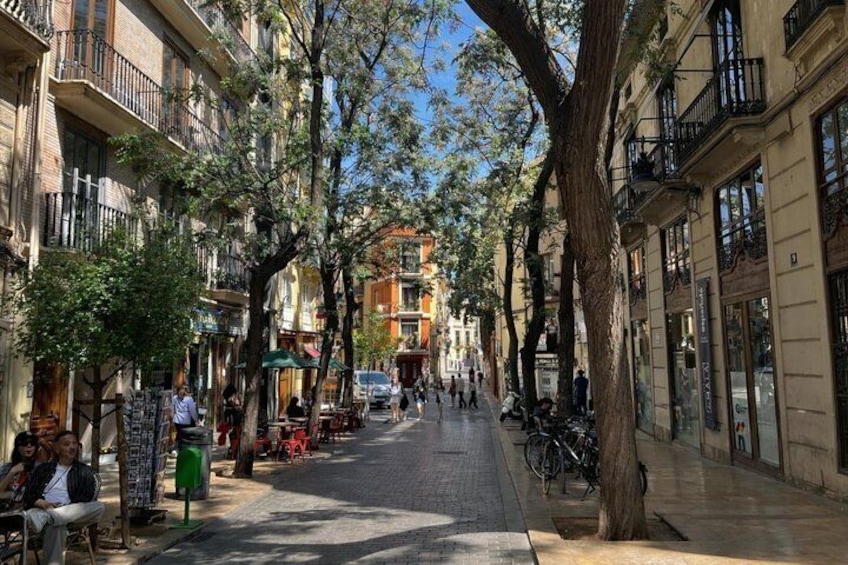 Una calle arbolada con edificios, bancos y gente caminando. 1