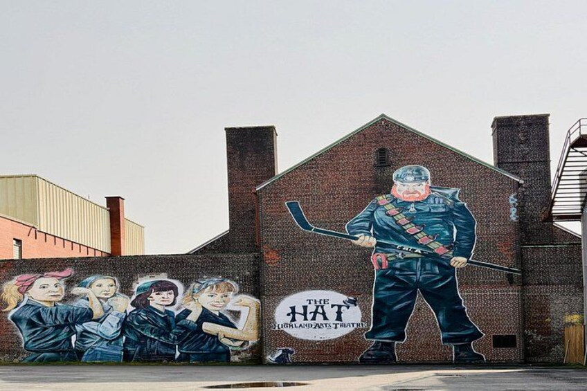 A mural on a brick building with a hockey player and a group of women. 2