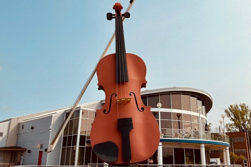 A large cello sculpture in front of a modern building with a curved facade and large windows. 3