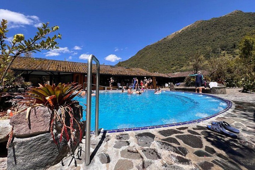 Une piscine où se baignent des gens, une terrasse en pierre et une montagne en arrière-plan. 1