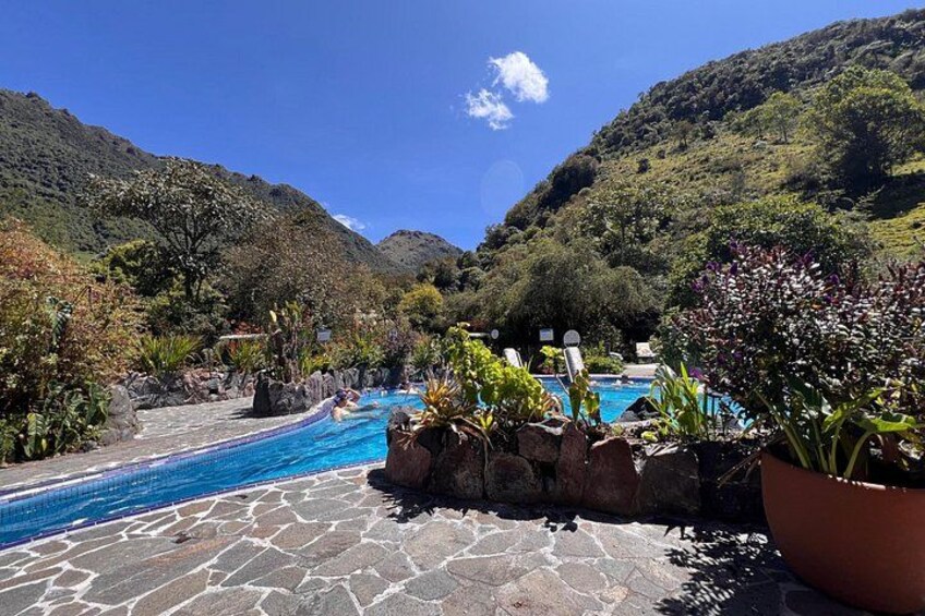 Une piscine bordée d’un chemin de pierre, entourée d’une végétation luxuriante et de collines. 5